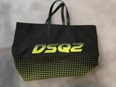 A black tote bag with two handles, featuring a yellow-green gradient 'DSQ2' logo on the front and a dotted pattern on the bottom half, set against a gray background.