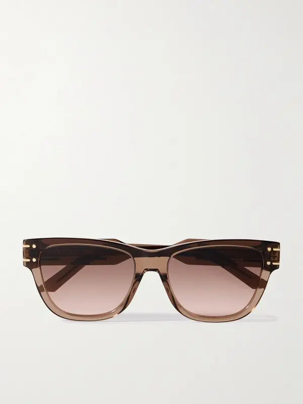 A pair of designer sunglasses with a translucent brown acetate frame and gradient brown lenses, featuring gold-tone rivet details on the temples, shown against a plain light background.