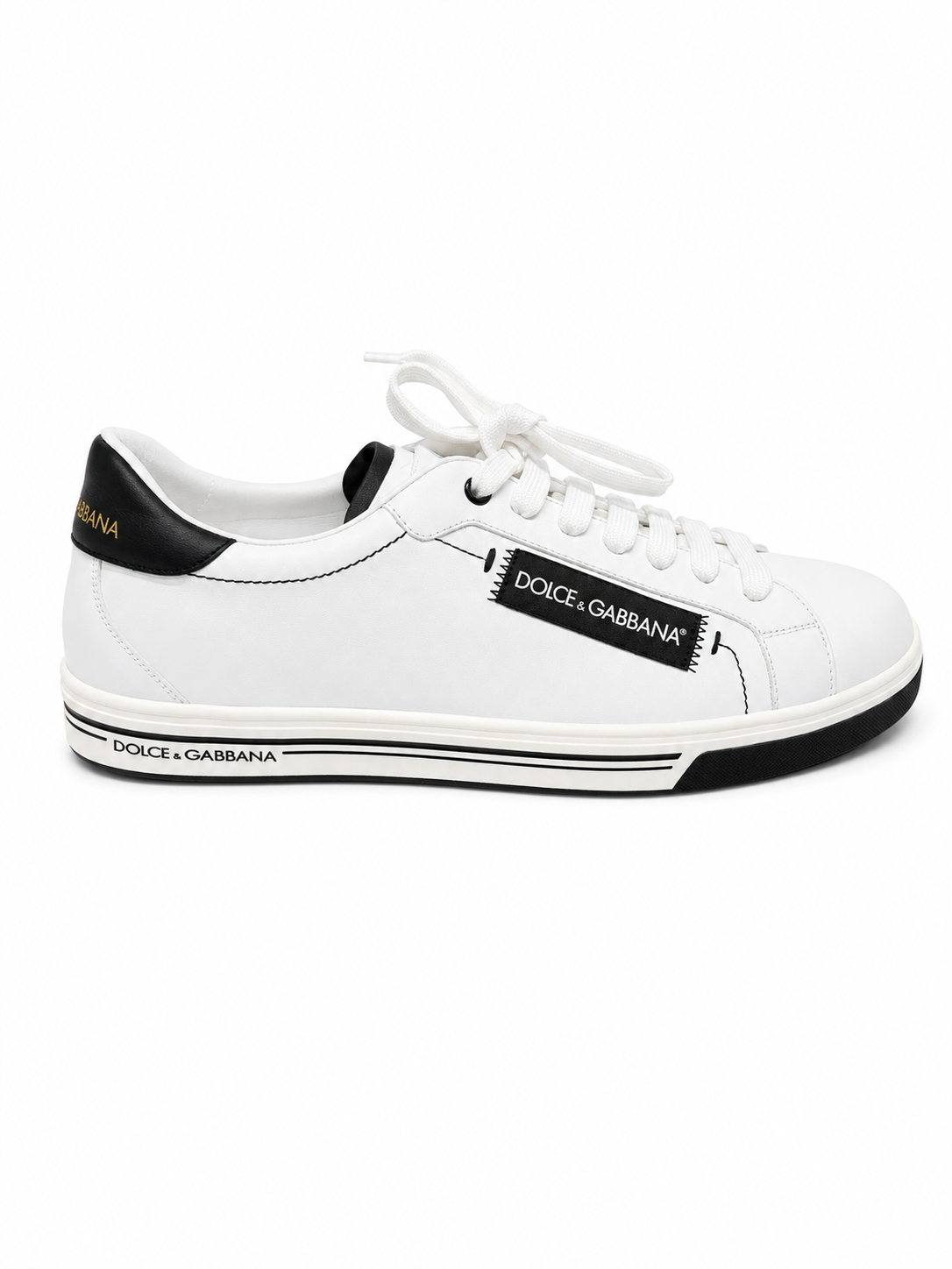 A white leather Dolce & Gabbana sneaker with black accents, featuring a black heel tab with gold lettering, a black side patch with white text, and a black and white striped midsole.